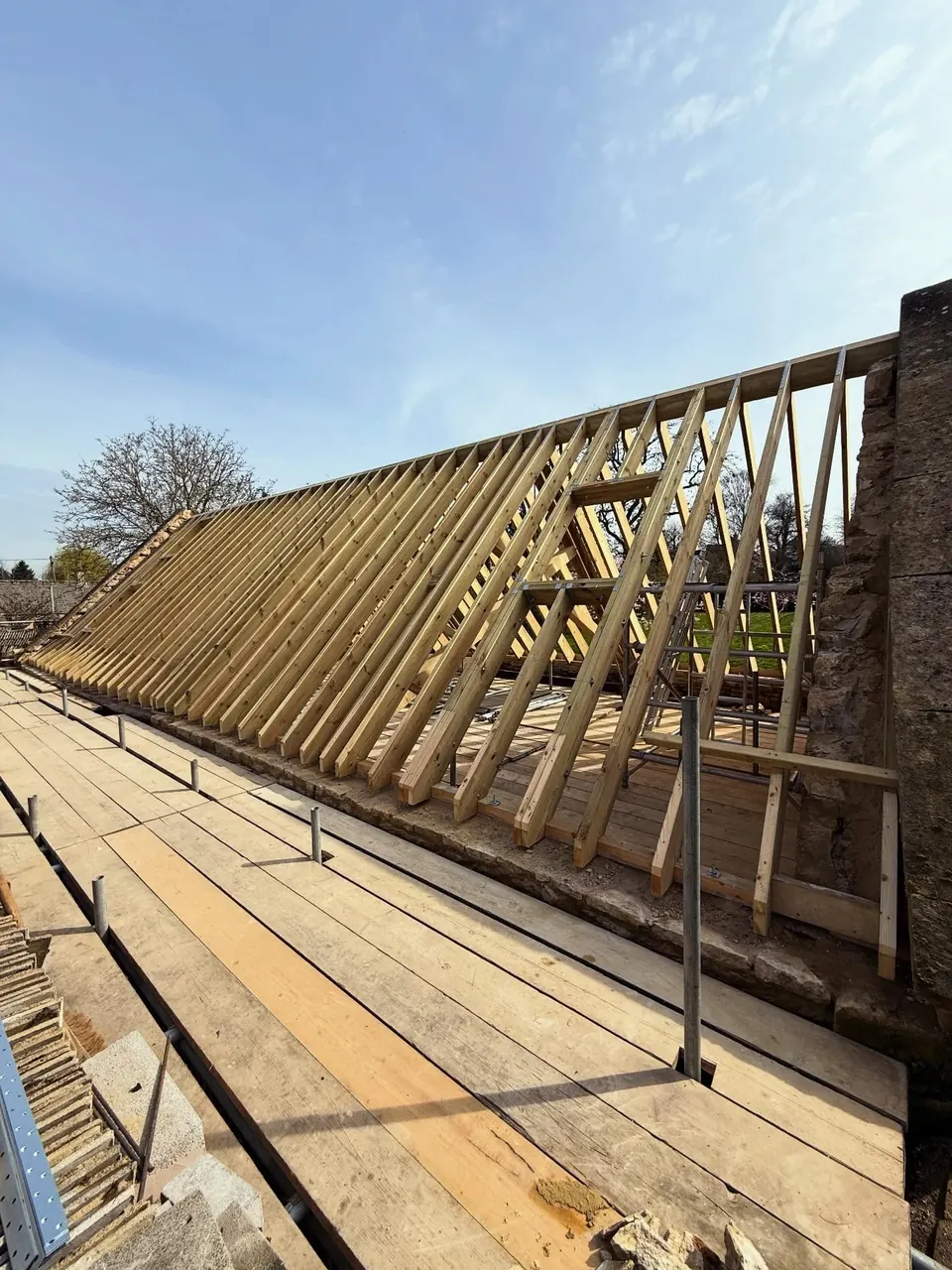 A long run of new rafters on the stone gable, with scaffold boards in the foreground