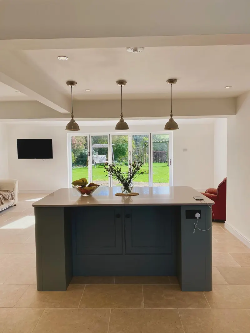 A new open-plan kitchen with a dark painted island, pendant lights and a garden view