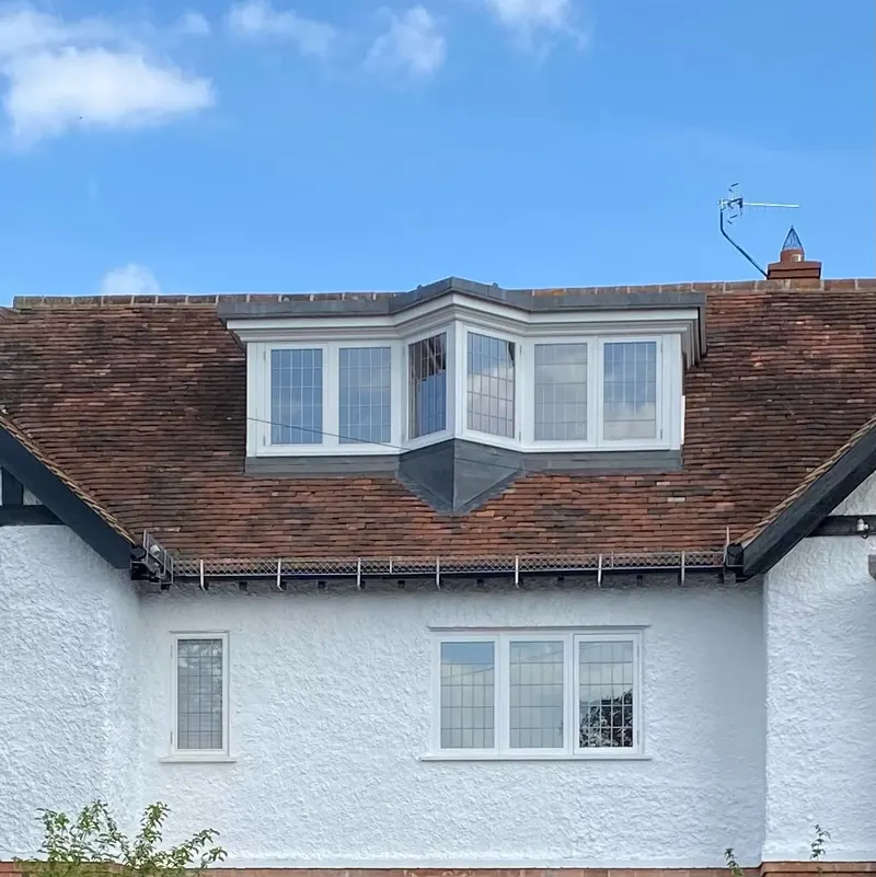 A birds-beak dormer window above a double bay window on a white rendered house