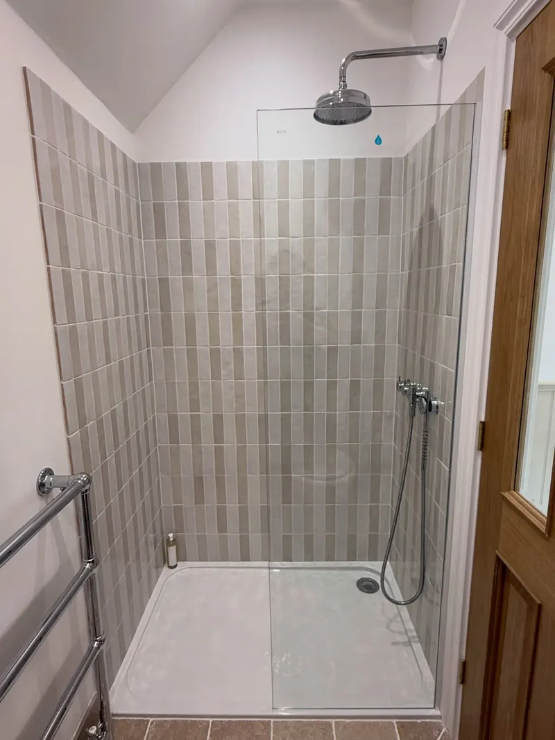 A tiled shower with stacked vertical tiles and a rain head beside an oak door