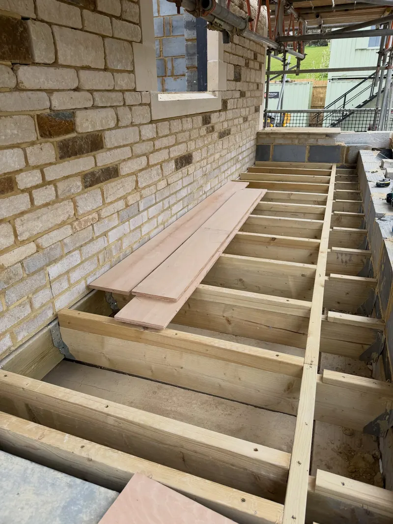 Joists and a stone parapet on a flat roof under construction, scaffolding overhead