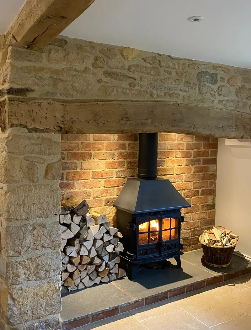 A restored stone inglenook with an oak beam, salvaged brick and a lit log burner