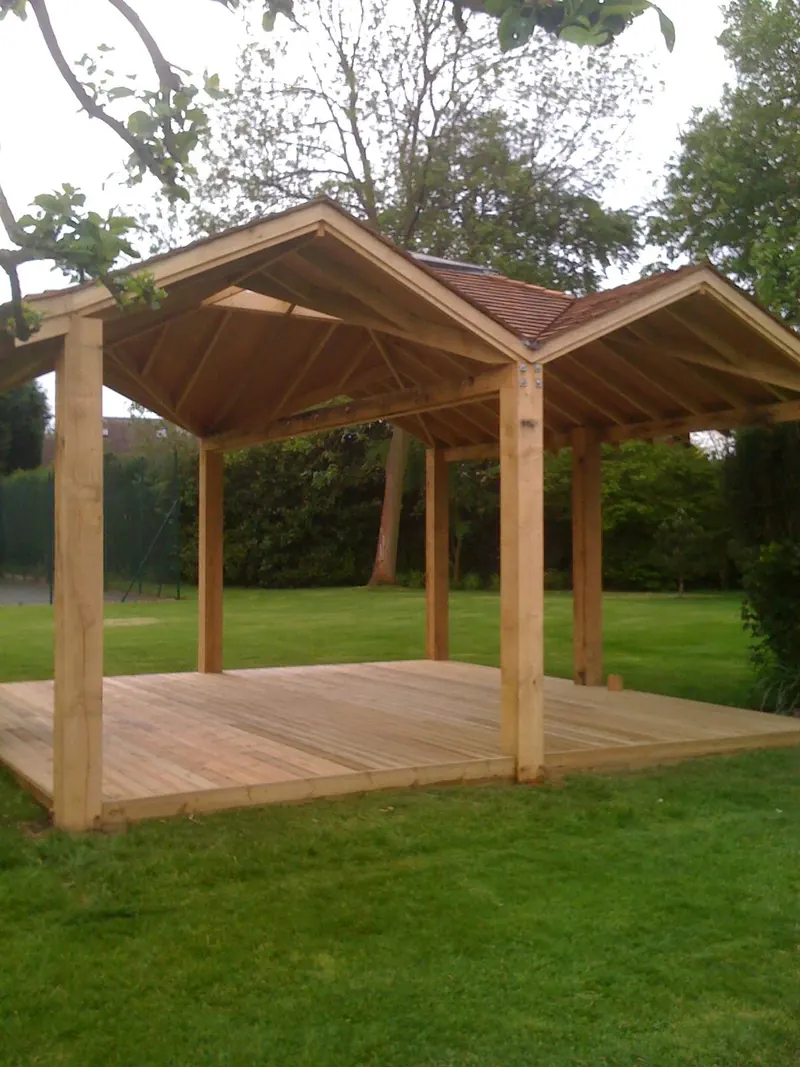 A green oak pavilion with two gables, cedar shingle roof and decking on a lawn